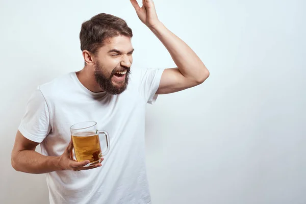 Homem com uma caneca de cerveja em suas mãos e um branco t-shirt luz fundo bigode barba emoções modelo — Fotografia de Stock