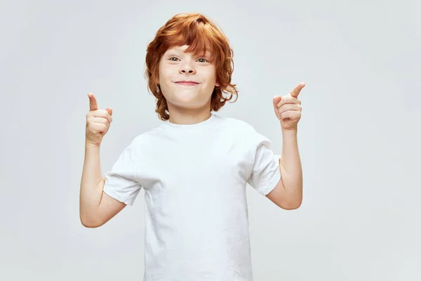 Веселий рудий хлопчик жестикулює руками індекс пальців посміхається біла футболка Копіювати Космос сірий фон — стокове фото