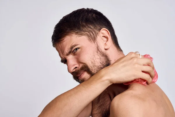 Muž s holými rameny a žínkou v rukou čistou pleť se sprchovým světlem na pozadí — Stock fotografie