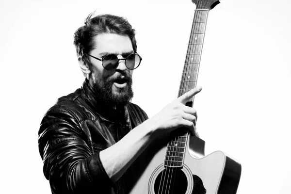 A man holds a guitar in his hands music emotions black leather jacket dark glasses studio light background