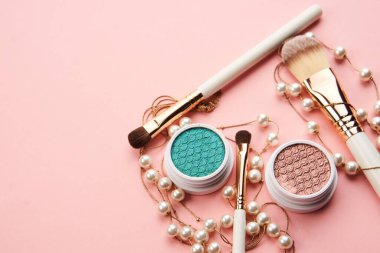 Göz falı aksesuarlar, boncuklar makyaj fırçaları pembe arka planda profesyonel kozmetik ürünleri koleksiyonu.