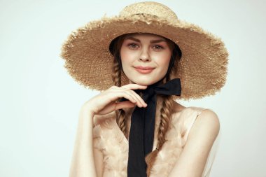 Hasır şapkalı, siyah kurdeleli ve arka planda açık bir elbise giyen hoş bir kız. Romantik bir model.