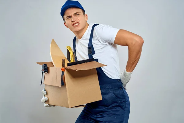 Muž v pracovní uniformě s krabicí v ruce nářadí nakladač dodání světlo na pozadí — Stock fotografie