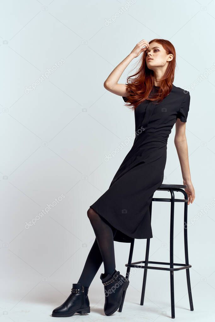 woman high chair indoors full length black dress red hair model boots