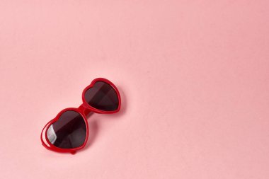 Kalp şeklinde güneş gözlüğü, pembe arkaplanda kırmızı çerçeveler.