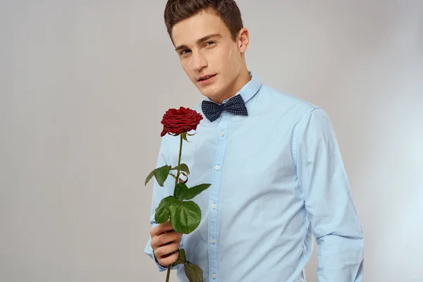 Romantikus férfi piros rózsával és kék ingben csokornyakkendővel a nyakában szürke háttér — Stock Fotó