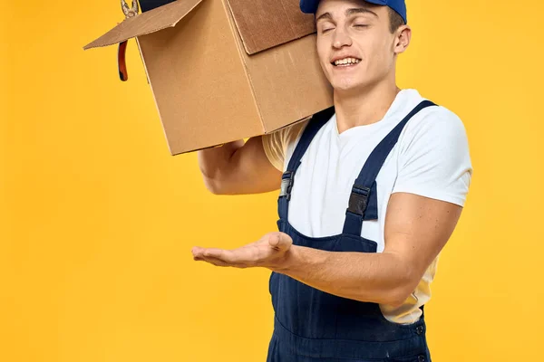 Kutu teslimat servisi sarı arka planda üniformalı bir işçi. — Stok fotoğraf