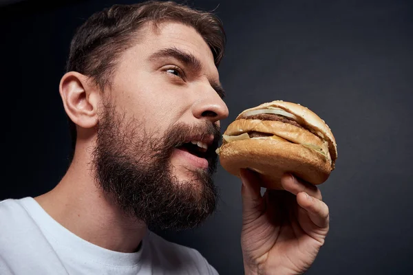 Férfi eszik hamburger gyorsétterem Gourmet étkezési sötét háttér — Stock Fotó