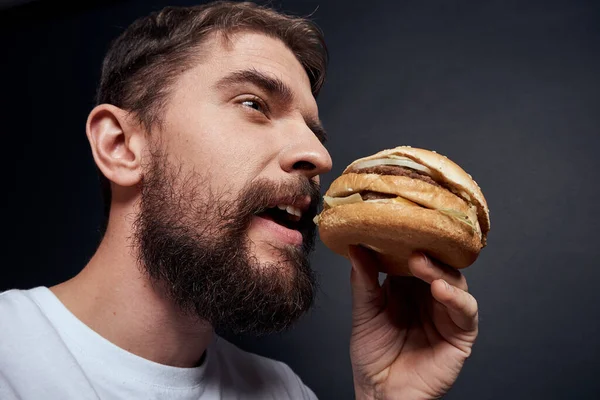 Hamburger yiyen fast food restoranı gurmesi karanlık arka plan yiyor. — Stok fotoğraf