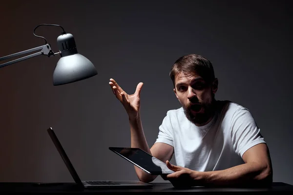 Man med bärbar dator sitter vid bordet mörk bakgrund arbetsplats kontor känslor lampa gest med händerna modell beskärd vy — Stockfoto