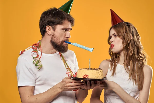 Man och kvinna födelsedag festlig tårta gul bakgrund och mössor på huvudet — Stockfoto