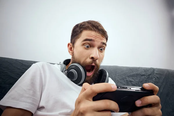 Ein Mann sitzt auf einem Sofa, ein Gamepad in der Hand. Freizeit-Lifestyle-Spielkonsole — Stockfoto