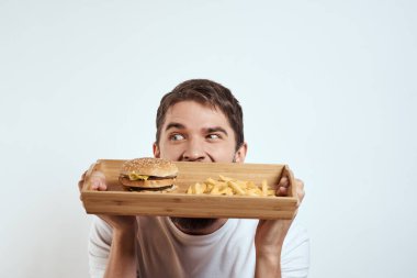 Ahşap tepside patates kızartması ve hamburger fast food kalorili beyaz tişört giyen bir adam.