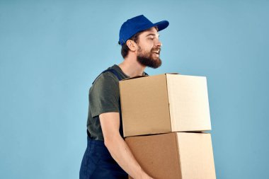 Elinde kutular olan işçi üniformalı adam teslimat servisinin mavi arka planında.