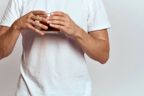 Un homme avec une boisson chaude de thé dans ses mains dans un T-shirt blanc sur un fond clair vue recadrée — Photo