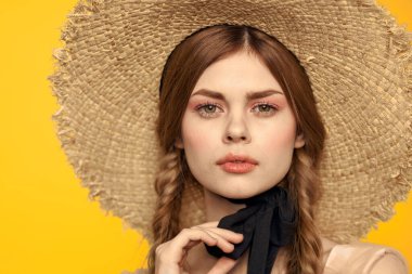 Şapkalı romantik bir kadın sarı arka planda eğleniyor ve güneş gözlüğü siyah kurdele modeli portresi takıyor.