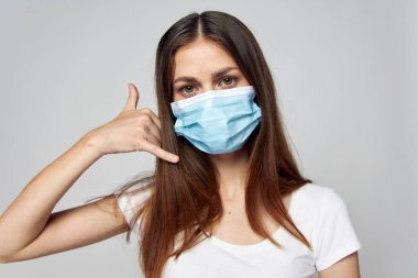 Yüzünde tıbbi bir maske olan esmer kadın elini hayat tarzının yakınında tutuyor. 