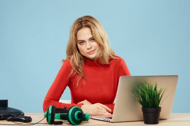 Dizüstü bilgisayar kulaklığının önündeki masada oturan bir kadın çevrimiçi yaşam tarzı mavi arka planda oynuyor.