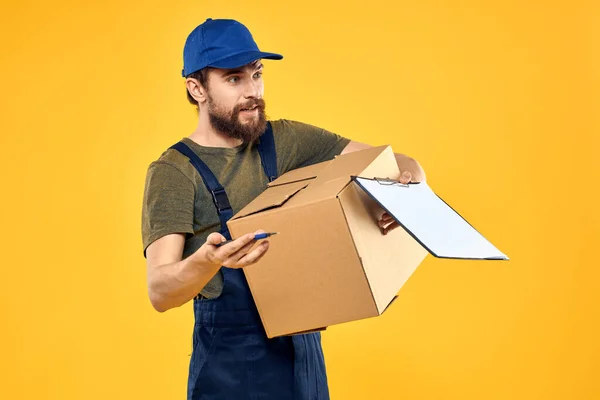 Pracovník kurýr doručuje krabice obaly dokumenty žluté pozadí — Stock fotografie