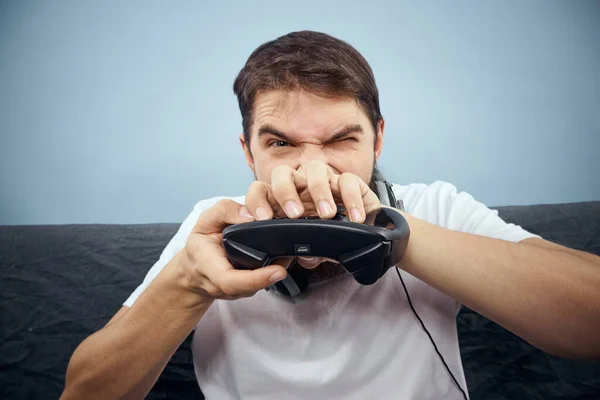 Un hombre se sienta en un sofá con un mando en la mano. Estilo de vida de ocio consola de juegos —  Fotos de Stock