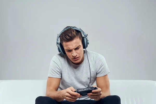 Un hombre con auriculares se sienta en el sofá de la consola de juegos móviles hobby entretenimiento —  Fotos de Stock