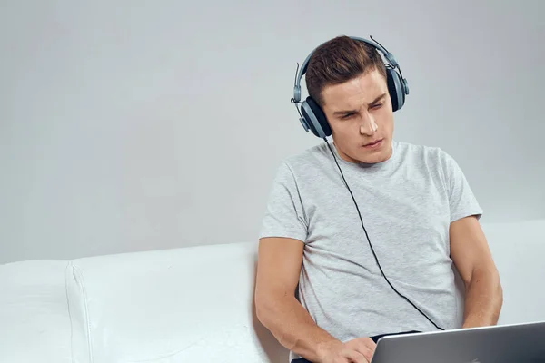 ビデオゲーム技術のヘッドフォンでジョイスティックを持つラップトップの前のソファの上の男 — ストック写真