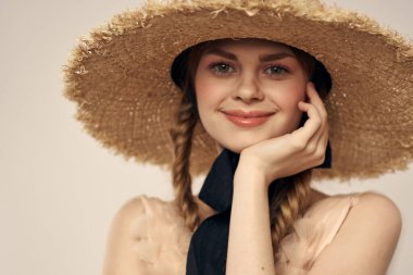 Hasır şapkalı, siyah kurdeleli ve arka planda açık bir elbise giyen hoş bir kız. Romantik bir model.