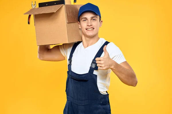 Kutu teslimat servisi sarı arka planda üniformalı bir işçi. — Stok fotoğraf