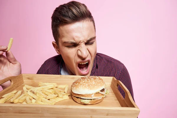 ファーストフードのある男食べるハンバーガーフライドポテトピンクの背景 — ストック写真