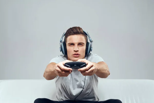 Een man in een koptelefoon zit op de bank mobiele spelcomputer hobby entertainment — Stockfoto