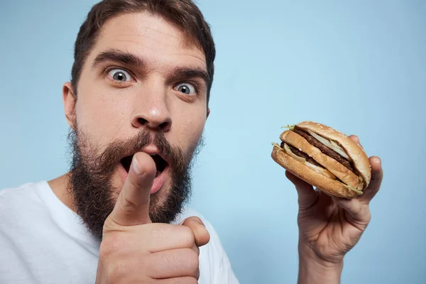 Emotionele man hamburger fast food dieet voedsel close-up blauwe achtergrond — Stockfoto