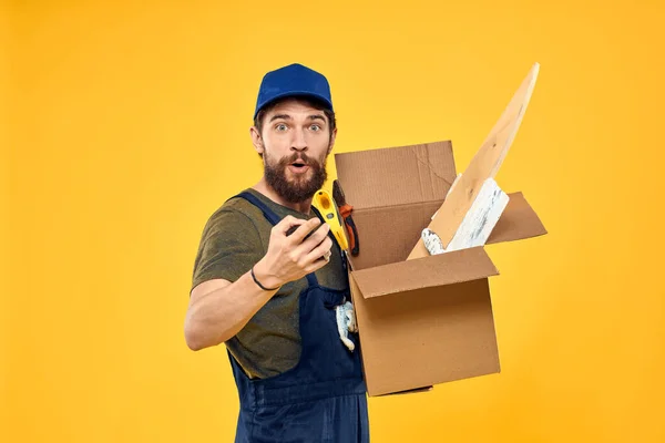 Ein Mann in einer Arbeitsform eine Box mit Ladewerkzeug gelben Hintergrund — Stockfoto