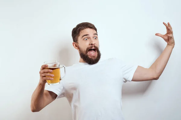 Hombre con una taza de cerveza en sus manos y una camiseta blanca fondo claro bigote barba emociones modelo — Foto de Stock