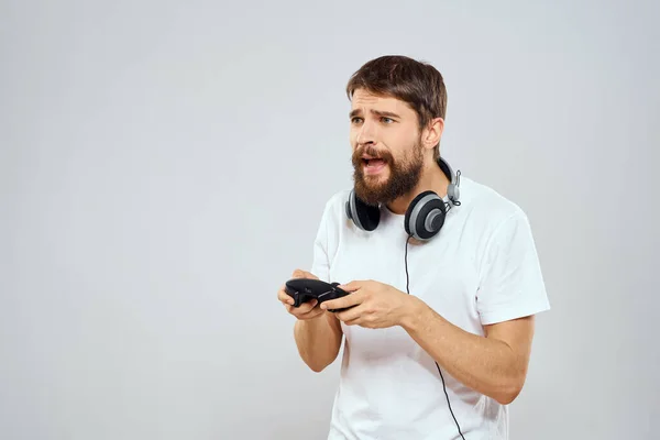 Hombre con auriculares gamepad jugando tecnología de ocio blanco camiseta fondo claro —  Fotos de Stock
