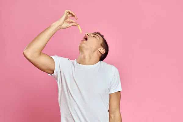 Lindo hombre con papas fritas en las manos emociones modelo de comida rápida rosa fondo recortado ver de cerca — Foto de Stock