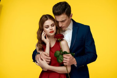 Aşıklar, ellerinde kırmızı bir gül, sarı arka planda romantik bir ilişkiye sarılıyorlar.