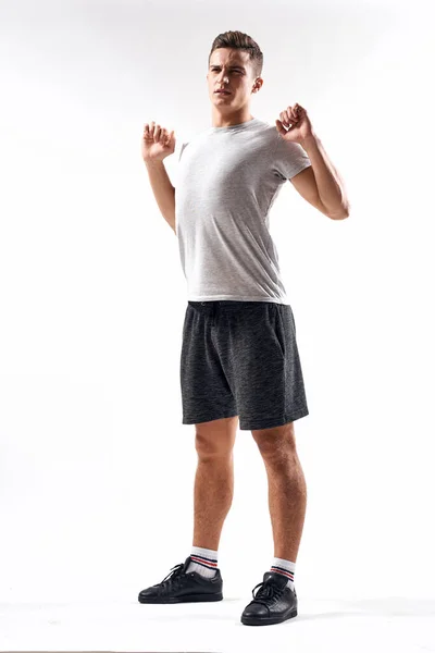 Un hombre deportivo en pantalones cortos y una camiseta larga hace ejercicios sobre un fondo claro — Foto de Stock