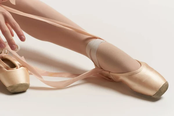 Ballerina mette scarpe da punta sui suoi piedi bianco nastro modello danza luce sfondo. — Foto Stock