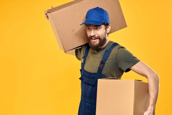En man i arbetsform en låda med laddningsverktyg gul bakgrund — Stockfoto