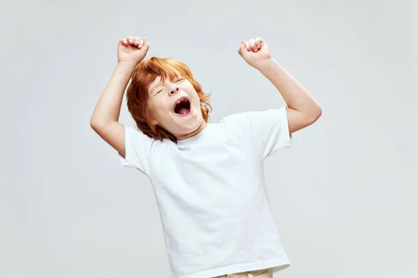 Redhead boy with open mouth holds hands above his head emotions white t-shirt cropped view