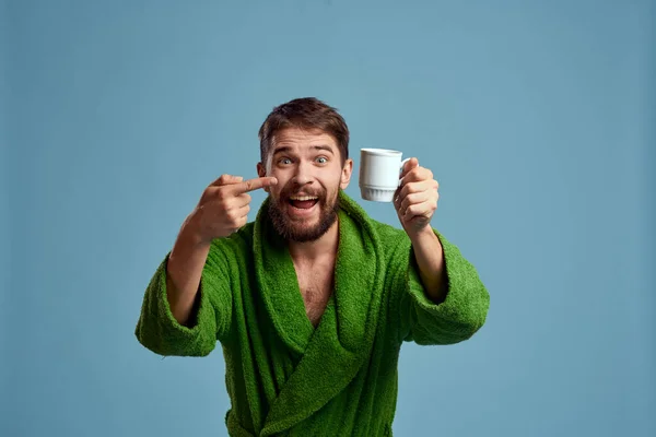 Homem congelado em um manto quente com uma xícara de bebida quente em um fundo azul vista cortada — Fotografia de Stock