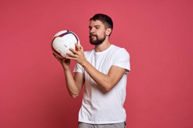 Pembe arka planda futbol topu olan bir adam. Elleriyle jestler yapıyor. Duygularını yönlendiriyor.