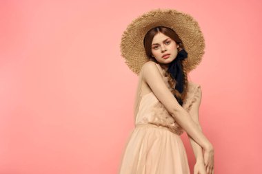 Pembe arka planda siyah kurdeleli şık elbiseli ve şapkalı bir kadın model duygularının eğlenceli görüntüsünü kırptı.