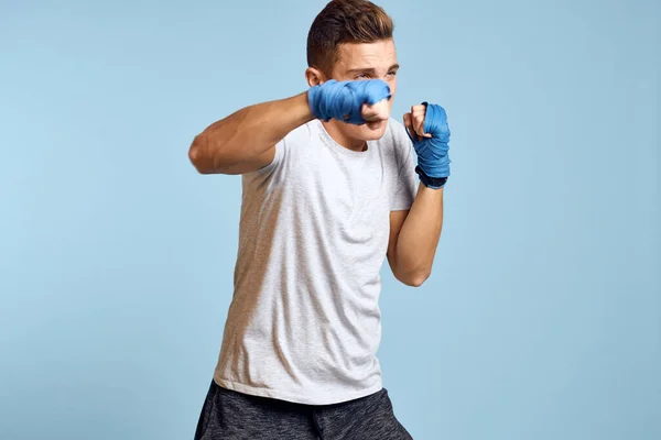 Sportovní muž v modrých boxerských rukavicích a tričku na modrém pozadí cvičení údery oříznutý pohled — Stock fotografie