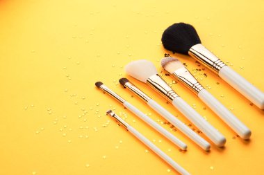 Sarı arka planda farklı boyutlarda makyaj fırçaları ve kırpılmış parıltılı görünüş