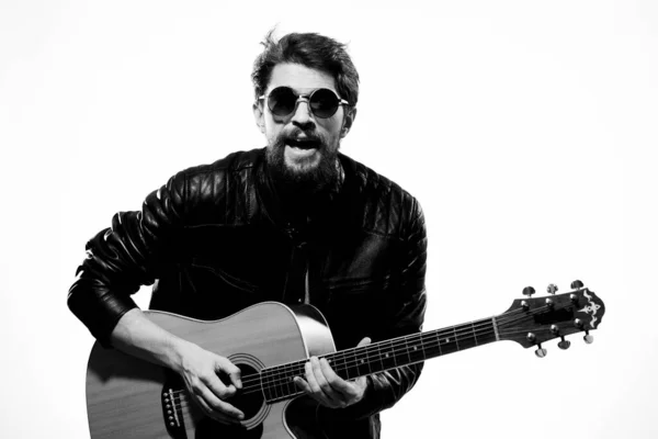 男が黒い革のジャケットでギターを弾き、サングラスをかけている。 — ストック写真