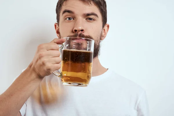 Un homme barbu avec une tasse de bière sur un fond clair dans un T-shirt blanc vue recadrée d'une boisson alcoolisée — Photo