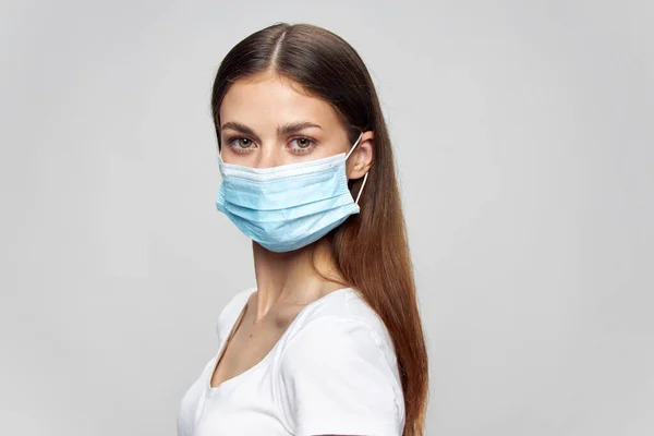 Kvinna i en vit T-shirt och i en medicinsk mask på en isolerad bakgrund porträtt — Stockfoto