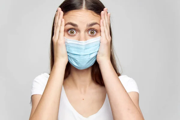 Verrast vrouw in medisch masker aanraken gezicht met handen en geïsoleerde achtergrond wit t-shirt — Stockfoto