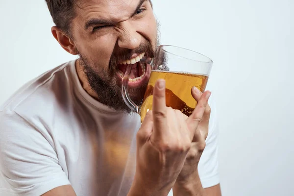 Ein bärtiger Mann mit einem Becher Bier auf hellem Hintergrund in einem weißen T-Shirt schnitt die Ansicht eines alkoholischen Getränks ab — Stockfoto